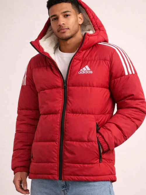 Front view of a man wearing a red Adidas quilted puffer jacket with a white sherpa-lined hood and signature white three stripes on the sleeves.