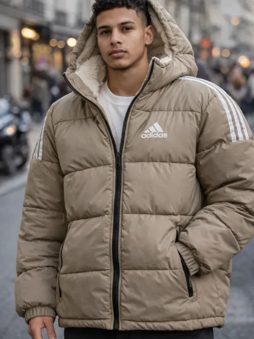 A man wearing an Adidas beige quilted puffer jacket with white three-stripe shoulder details and a soft cream sherpa-lined hood in an urban city street.