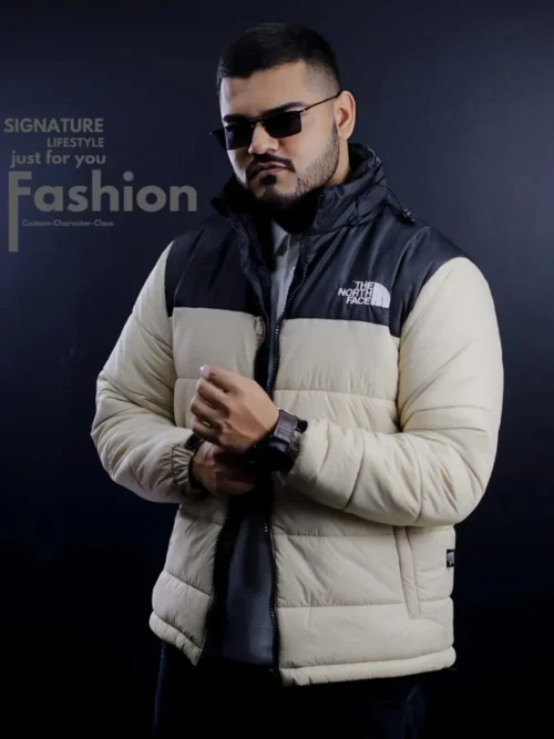 A man wearing a stylish The North Face quilted puffer jacket in a two-tone cream and black color scheme with a signature logo on the chest.