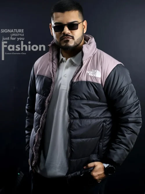 A man modeling a The North Face Retro Nuptse puffer jacket featuring a black body and mauve pink shoulders, paired with a white polo shirt and black sunglasses.
