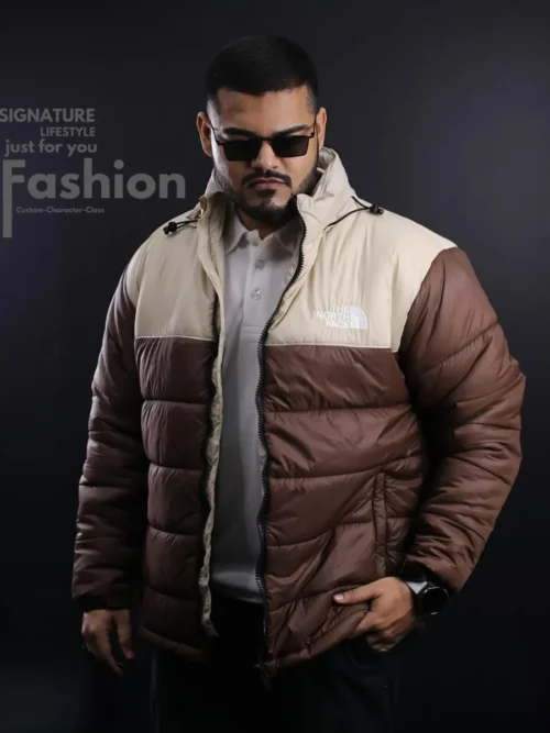 A man wearing a premium The North Face insulated puffer jacket in a chocolate brown and cream beige colorway with a white embroidered logo and adjustable stand-up collar.