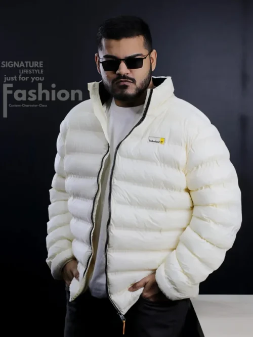 A man modeling a premium Timberland off-white quilted puffer jacket featuring a high collar, black zipper, and brand logo on the chest.