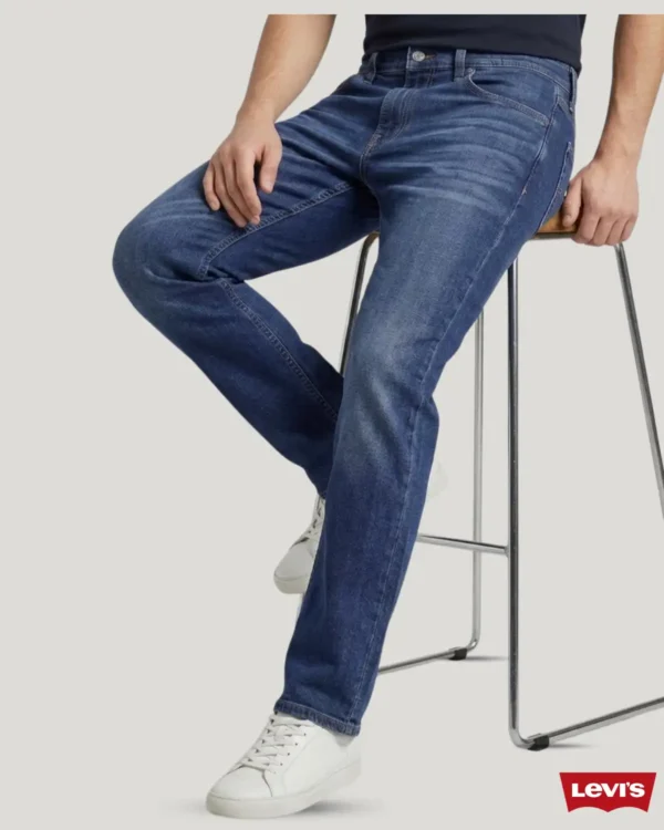 A mode showcasing deep blue color jeans sitting on a chair posing like model to show the jeans pant