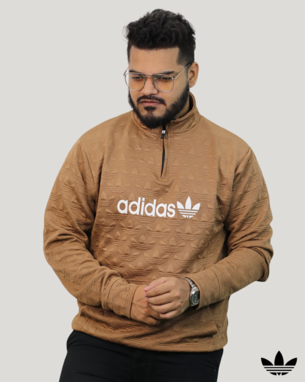 A young man wearing a brown half-zip sweatshirt featuring a textured all-over pattern, a large white logo on the chest, and a front pocket. Signature Lifestyle men's winter fashion in BD.