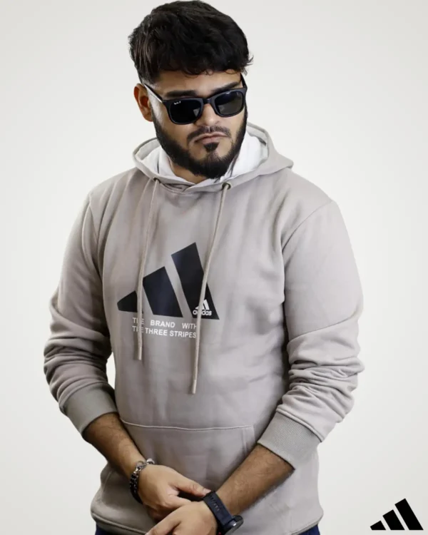 Model posing in a light beige khaki men's fleece hoodie with a modern black graphic print on the center chest, long sleeves with ribbed cuffs, and a cozy double-layered hood.
