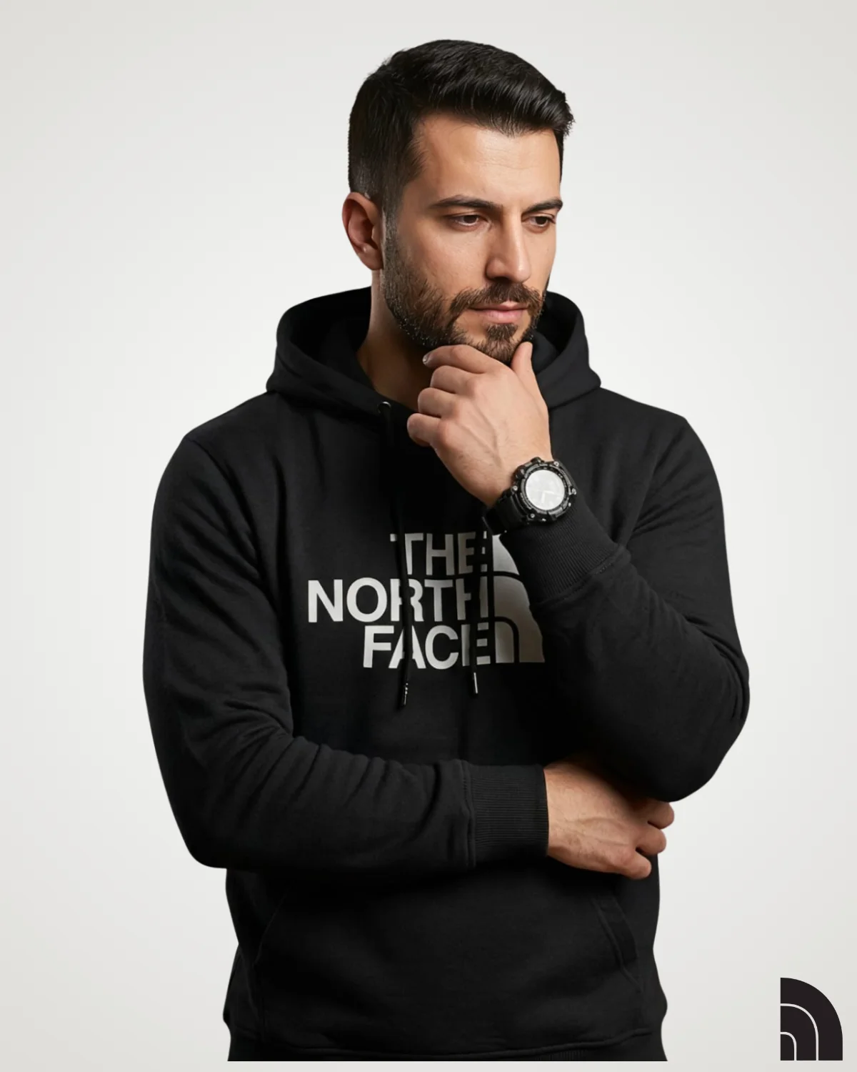 A bearded male model posing in a premium black classic mens hoodie, featuring a large white geometric text print across the chest, adjustable drawstrings, long ribbed sleeves, and a comfortable kangaroo pocket.