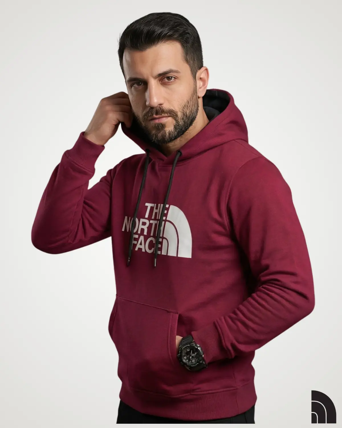Side-angle shot of a man wearing a dark maroon classic mens hoodie, showcasing a clean white graphic print on the front, double-layer hood with black drawstrings, and hands tucked into a front kangaroo pocket.