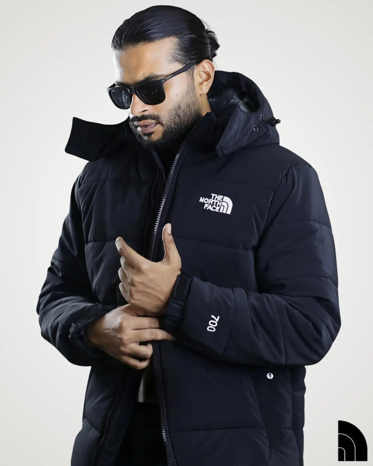 Front view of a man modeling a thick black 700 fill sherpa fleece jacket with a protective hood. This premium winter outerwear features a full zip-up front, adjustable velcro cuffs with numeric embroidery, and a white embroidered logo on the chest, offering ultimate warmth and street-style fashion.