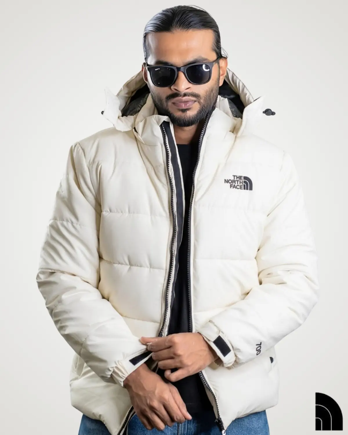 Front-facing view of a trendy man dressed in a cream-colored 700 fill sherpa fleece jacket. This bright insulated winter apparel features a high neck collar with an attached hood, striking black zipper details, and a soft, warm exterior for stylish winter layering.