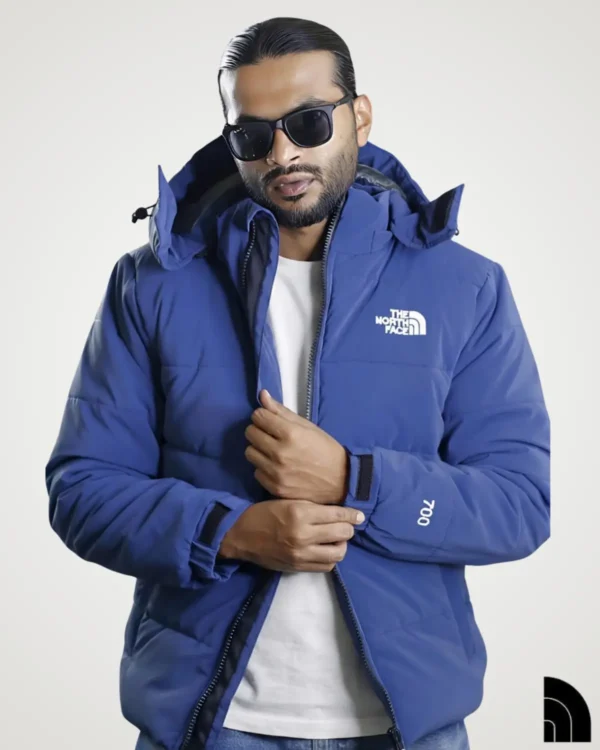 Portrait of a model posing in a vibrant navy blue 700 fill sherpa fleece jacket worn casually over a white t-shirt. The image highlights the jacket's thick insulated texture, adjustable hood, and contrasting zipper, perfect for outdoor winter activities.