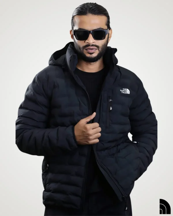Tall Model with hands in pockets wearing a midnight black lightweight down jacket for men, designed with horizontal quilted baffles, a protective hood, and dark zipper detailing.