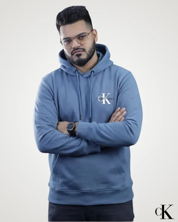 Front view of a man posing with folded arms in a premium steel blue Export Quality Pullover Hoodie, designed with a small contrast logo printed on the left chest and a double-stitched kangaroo pocket.