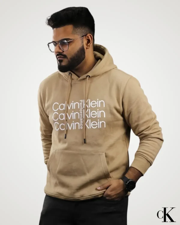 Model wearing a light beige mustard brown Export Quality Pullover Hoodie, styled with stacked white text graphic print across the center chest, long sleeves with fitted cuffs, and matching drawstrings.