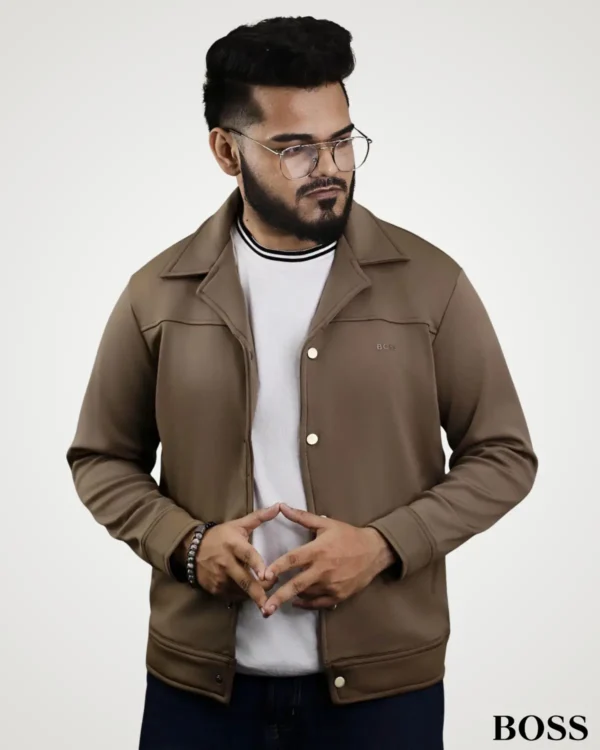 Front view of a model posing in a olive-brown suede leather jacket for men, styled with a classic shirt collar, front metallic snap buttons, and long cuffed sleeves.